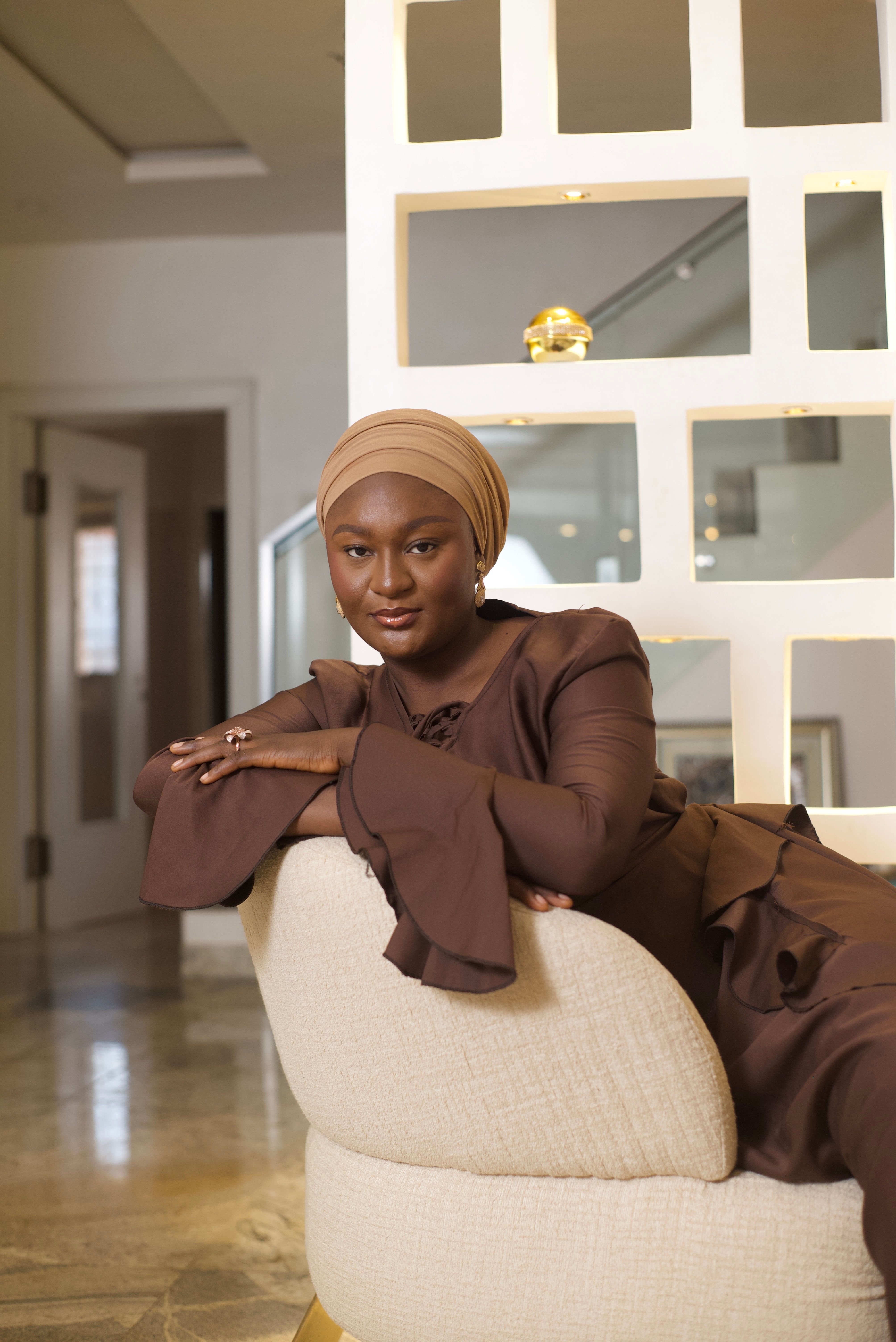 Portrait of a stylish Nigerian woman in elegant brown attire, showcasing traditional fashion indoors.