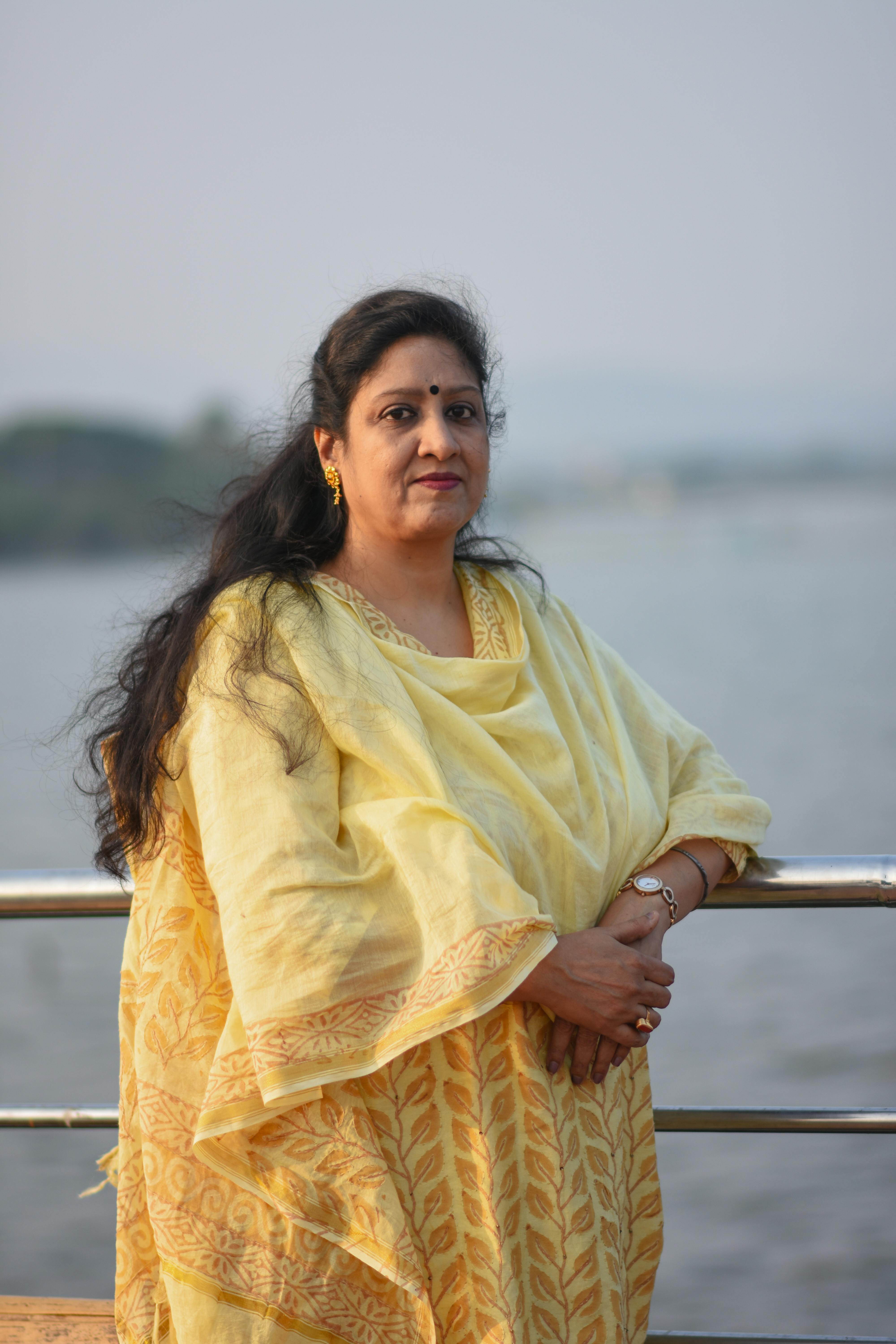 Portrait of a South Asian woman in a yellow saree standing by the river, showcasing elegance and cultural charm.
