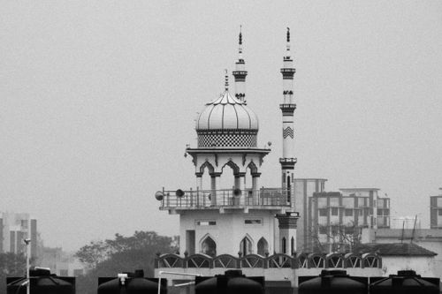 Free Black and white photo of a mosque minaret amidst a cityscape, featuring intricate architectural details. Stock Photo