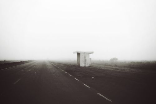 Free A scenic view of an empty highway shrouded in fog with a lone bus stop. Stock Photo