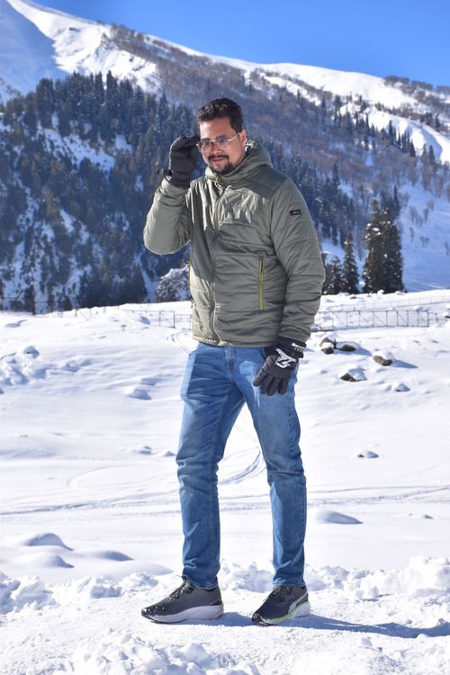 Free Man in winter jacket stands confidently in snowy mountains with blue sky. Stock Photo