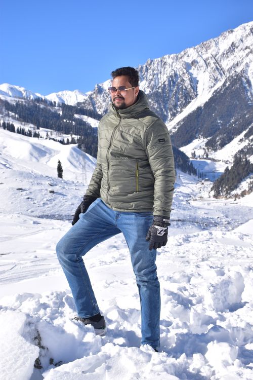 Free Man in warm clothing stands confidently on snowy mountain with clear blue sky. Stock Photo