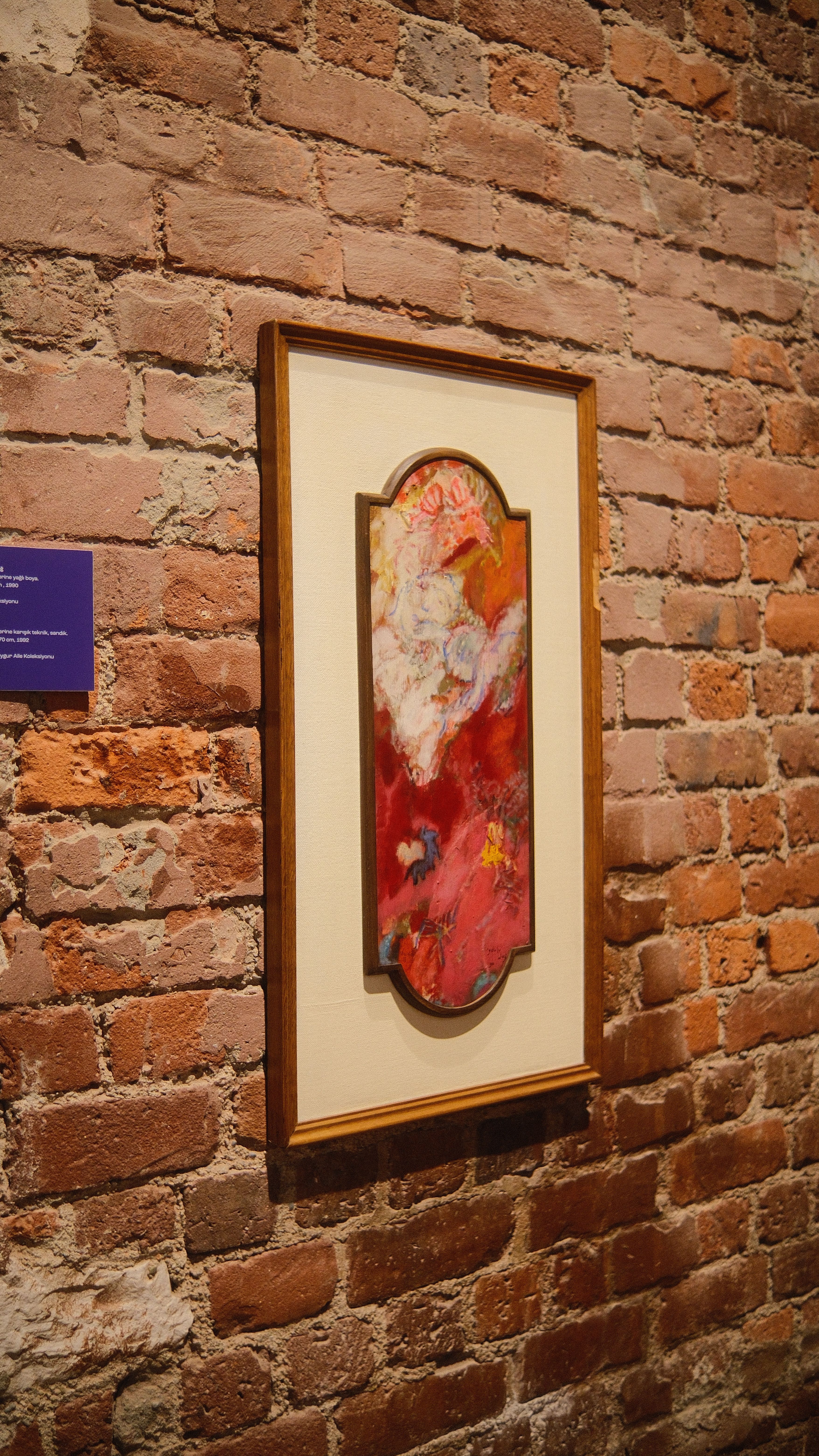 Abstract painting with vibrant colors displayed on a brick wall indoors.