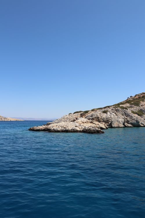 Free Tranquil image of the rocky coastline at Agistri, Greece, with clear blue waters under a bright sky. Stock Photo