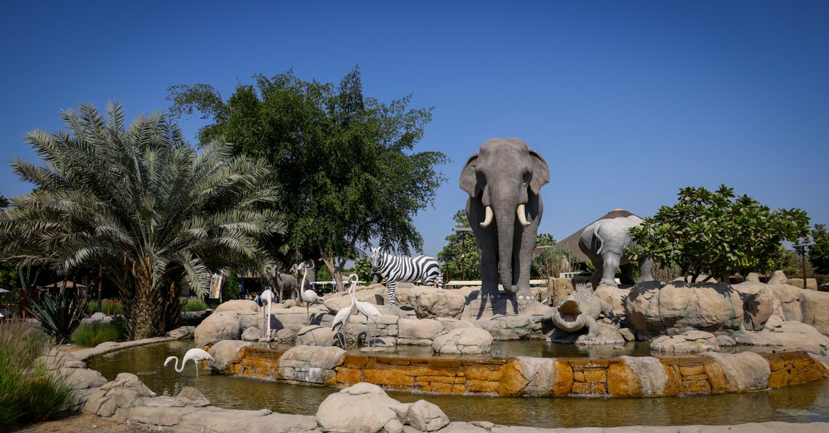 Outdoor zoo exhibit with animal statues set in natural scenery.