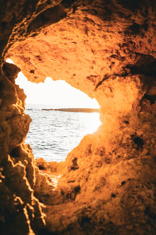 Free Scenic view of the ocean through a coastal cave in Portugal at sunset, capturing warm golden tones. Stock Photo