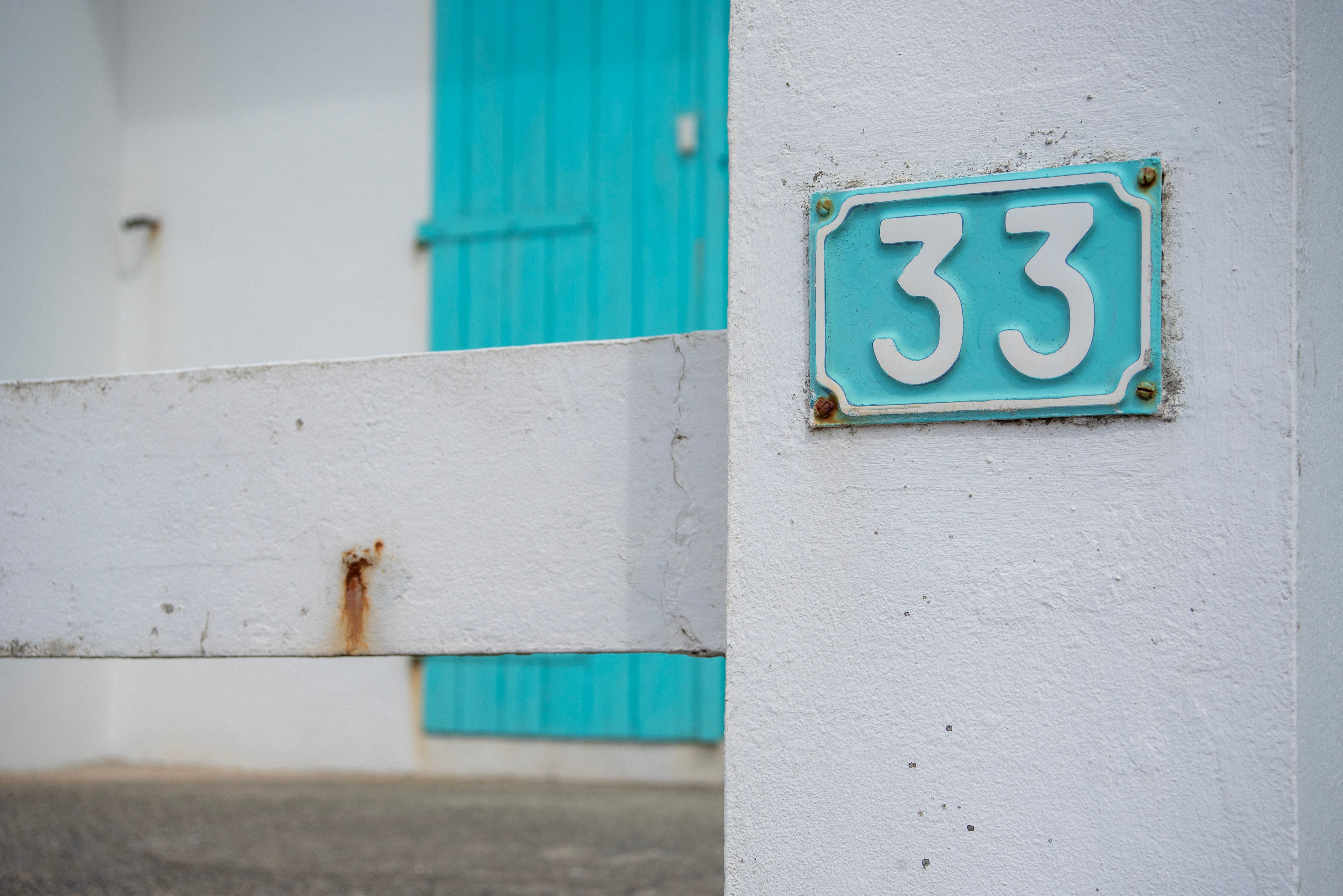 A rectangular, teal-colored metal house number plate with the white digits 