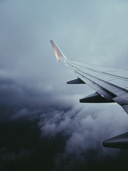 View of an airplane wing flying through dramatic cloudy skies, showcasing a serene mid-flight moment.