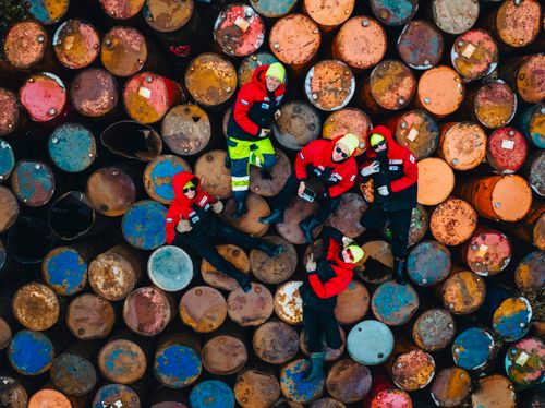 Free Aerial shot of people in red jackets resting on colorful rusty oil drums, showcasing a unique industrial setting. Stock Photo