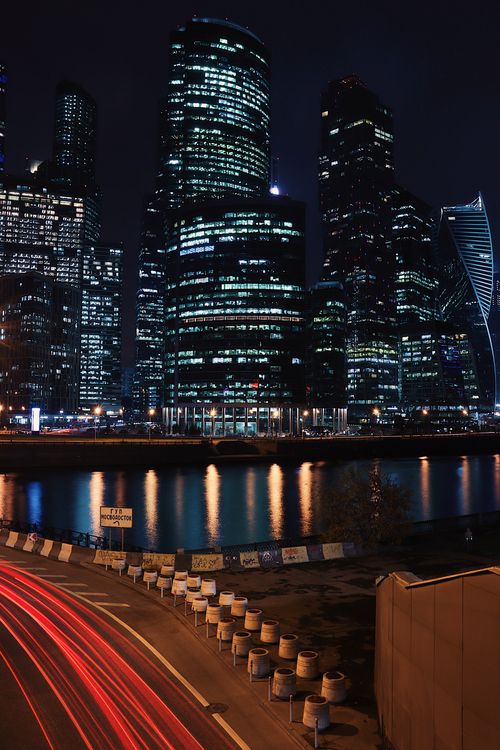 Free Dazzling night view of Moscow City skyscrapers reflecting in the river with light trails on a nearby road. Stock Photo
