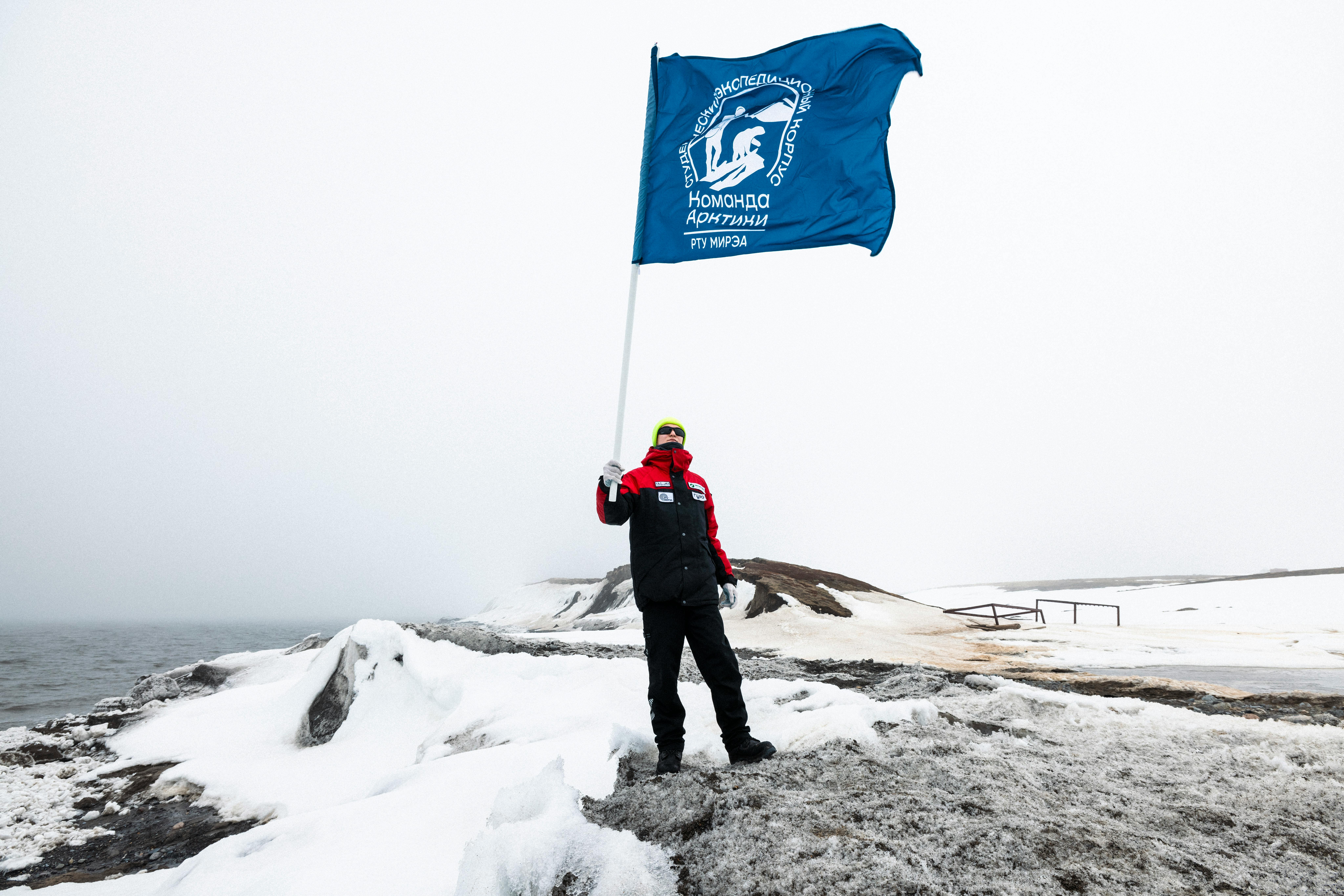 Man holding a flag in the Arctic landscape, showcasing exploration spirit.