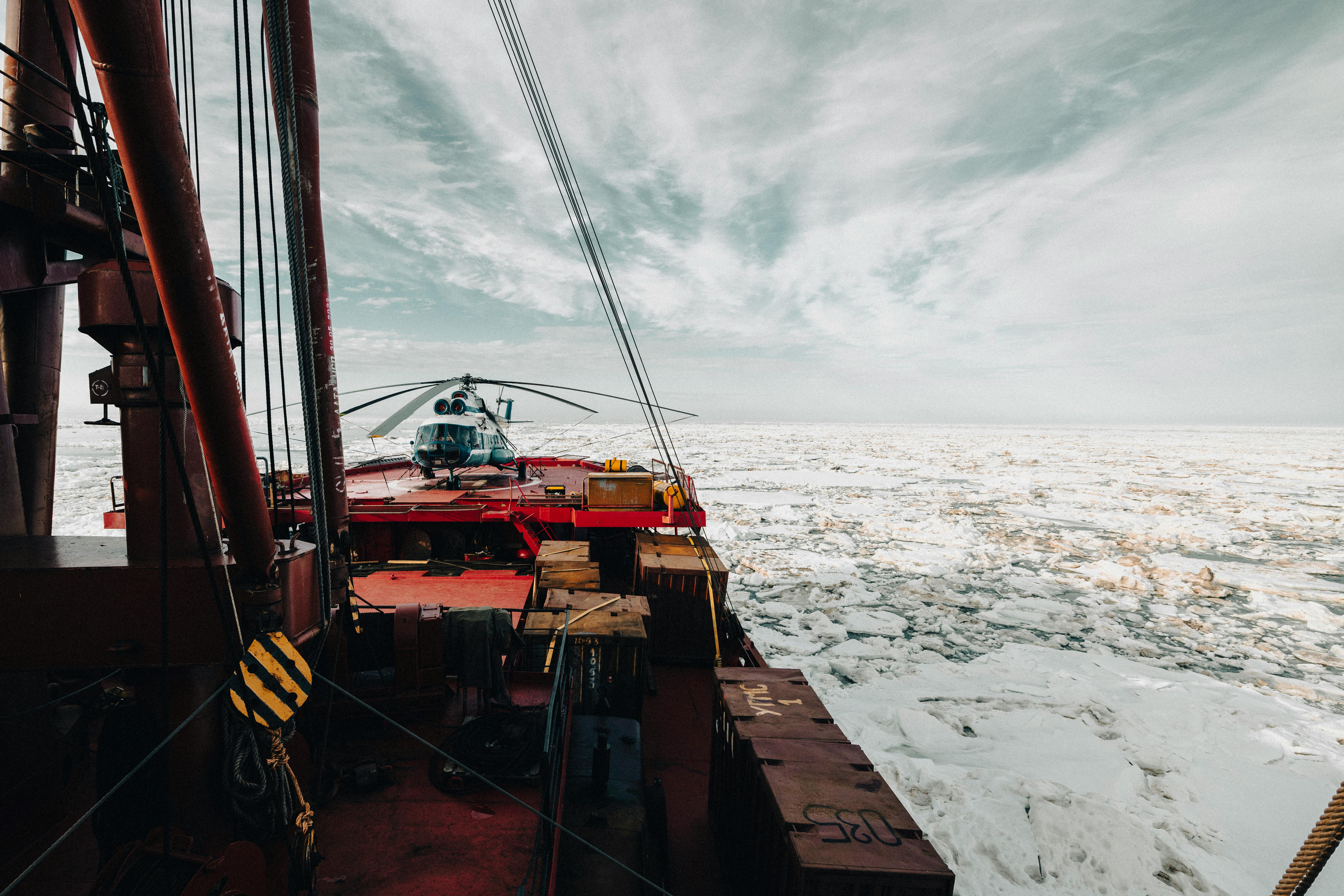 A helicopter on the deck of an icebreaker ship navigating through icy Arctic waters.
