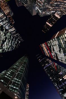Upward view of modern skyscrapers with lights, framing a night sky star shape.
