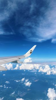 Aerial view from airplane cockpit, flying above fluffy clouds under a vibrant blue sky.