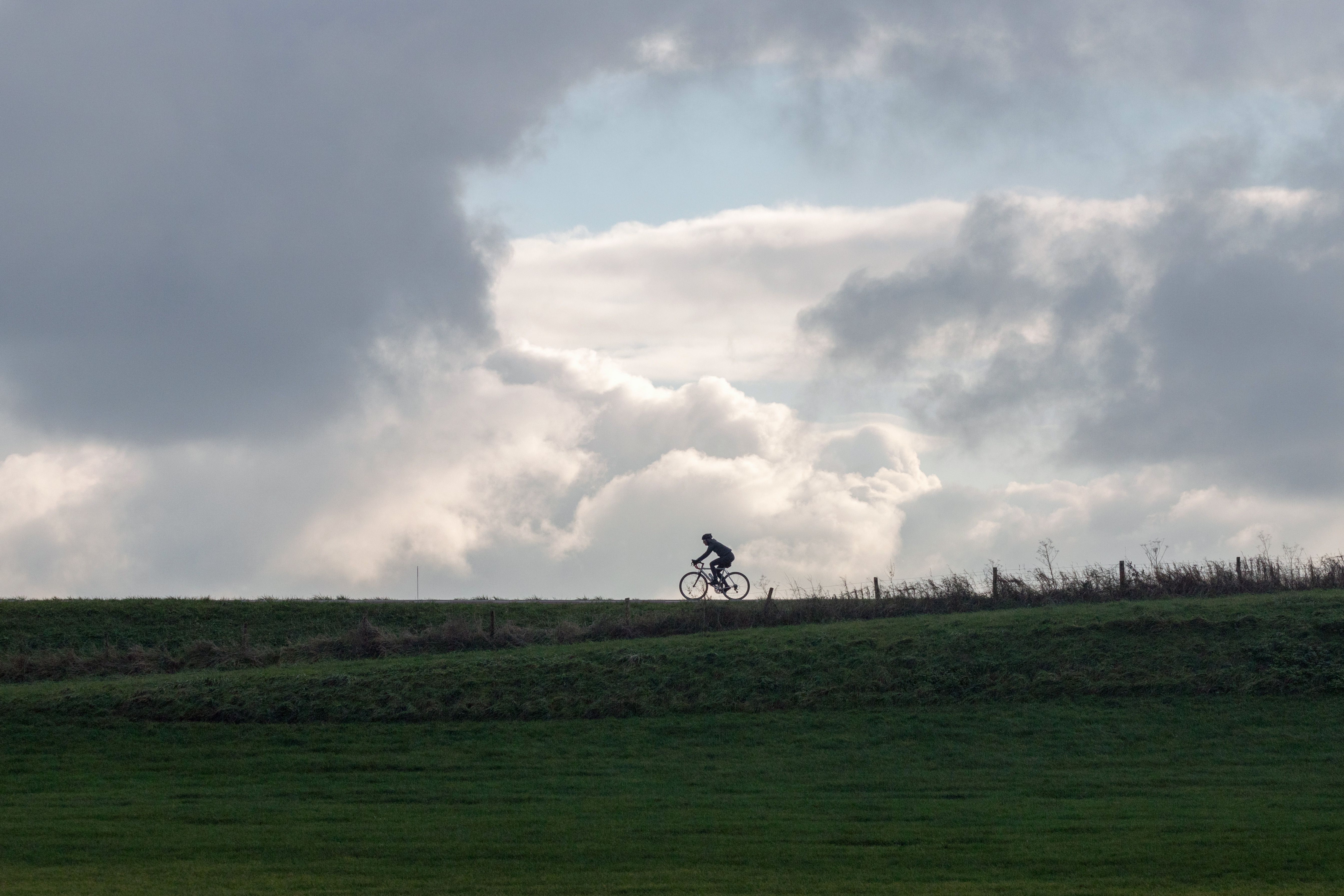 Cyclist riding on a hill in Nederland with clouds overhead, creating a dramatic silhouette effect.