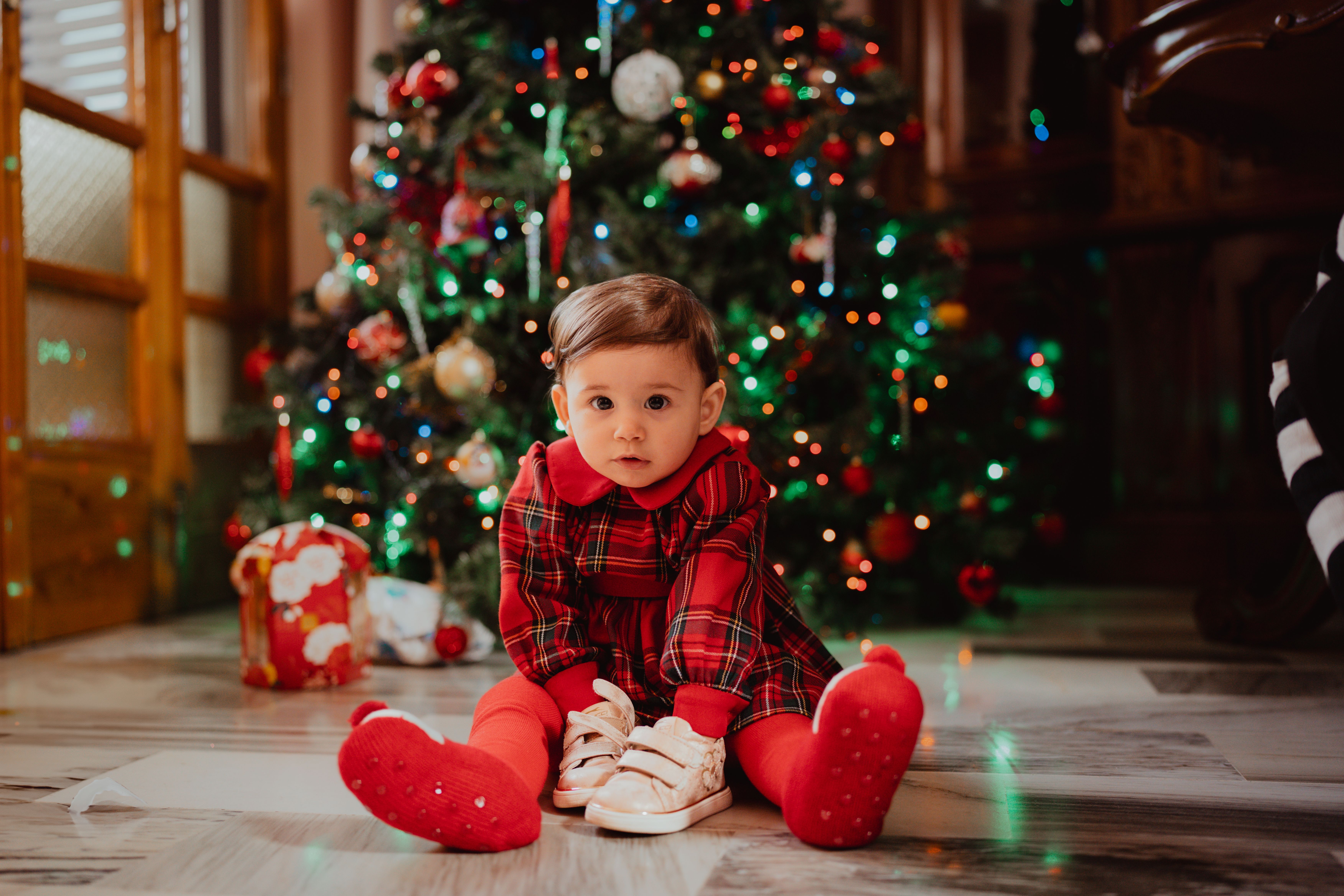 baby in holiday outfit sitting near a decorated christmas tree