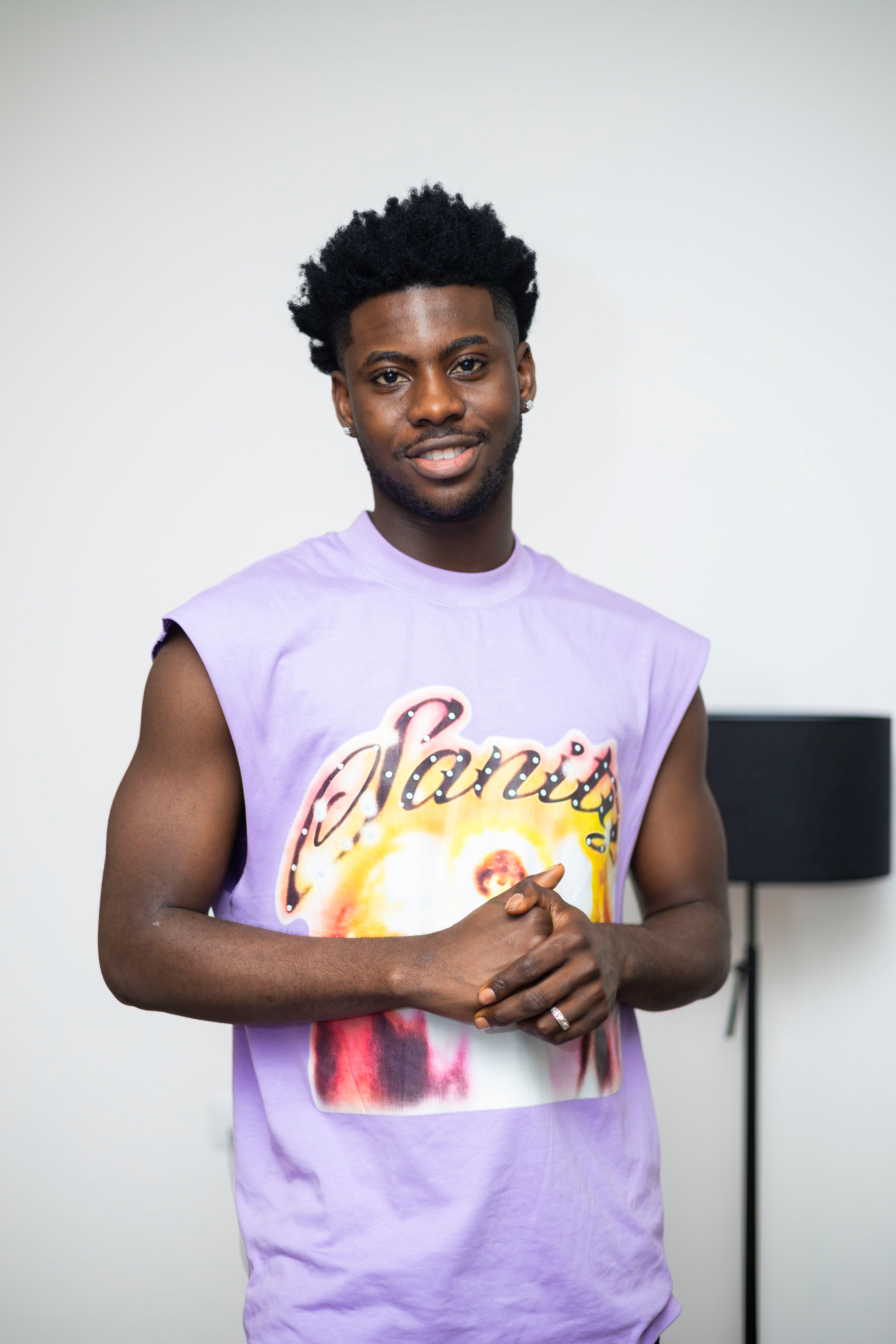 Casual portrait of a confident young man in a purple shirt indoors, smiling at the camera.