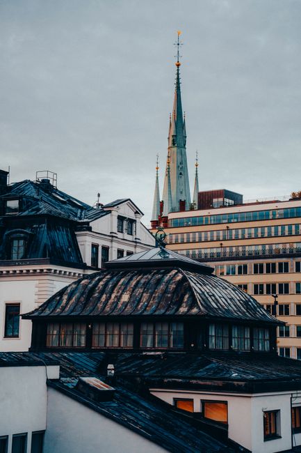 Dramatic view of Stockholm rooftops with a historic spire against a cloudy sky.