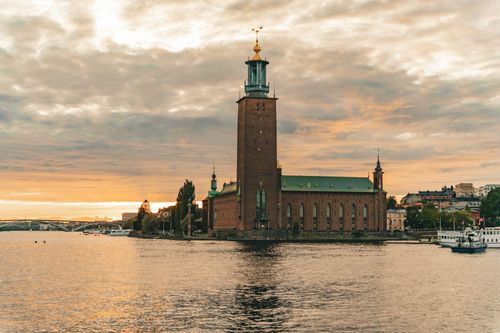 View of the iconic Stockholm City Hall during sunset, reflecting over the water in Stockholms län, Sweden.
