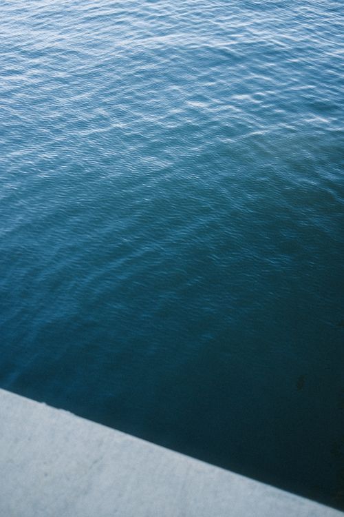 Free Peaceful blue ocean water viewed from a concrete edge, ideal for backgrounds or texture. Stock Photo