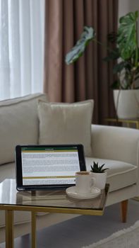 Stylish living room with a tablet, coffee, and plant on a glass table. Cozy and modern.