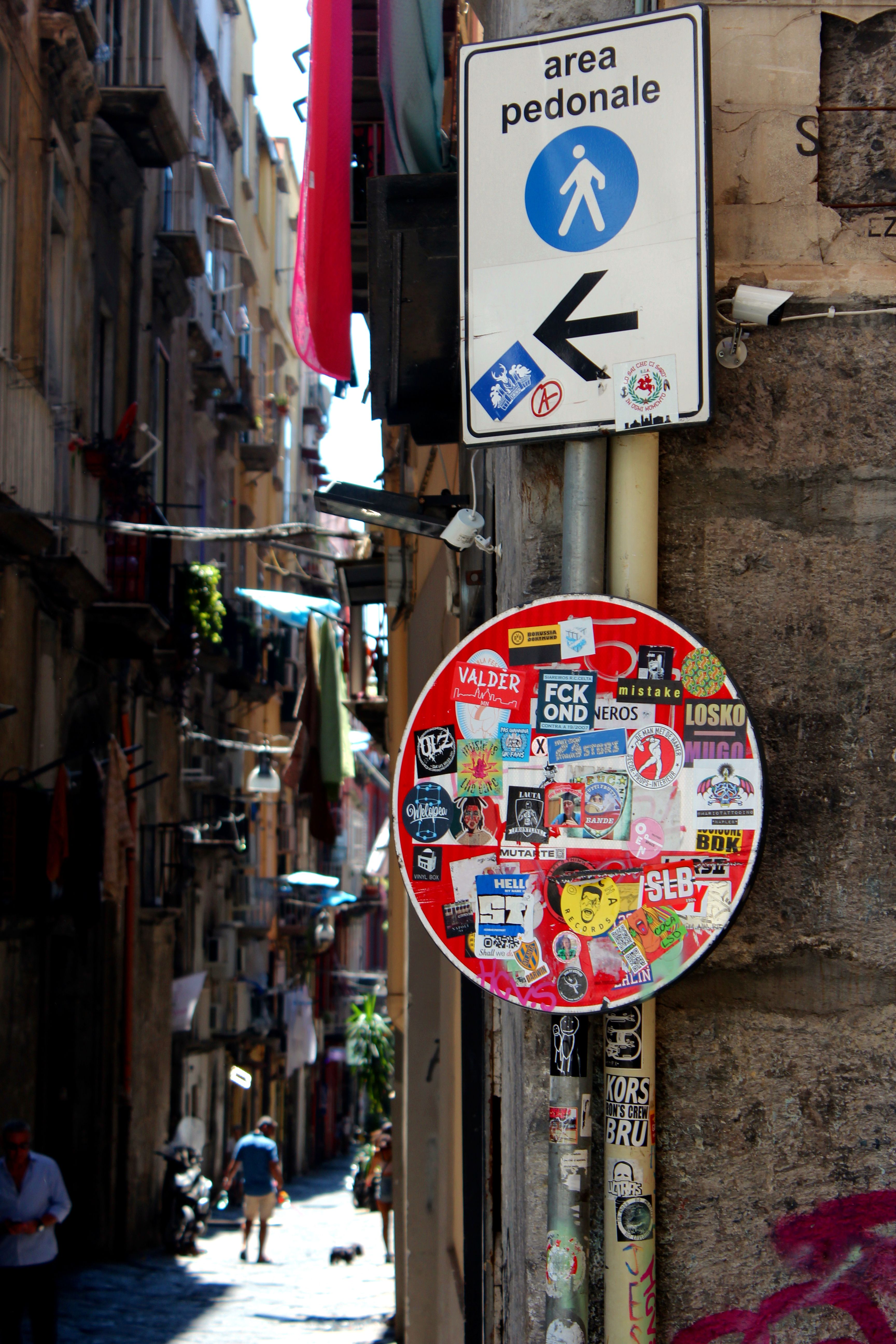 A pedestrian area sign with stickers in a narrow Italian street, capturing the lively urban vibe.