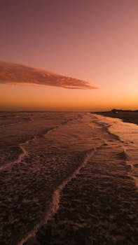 A beautiful view of the ocean during sunset with soft waves and a warm gradient sky.