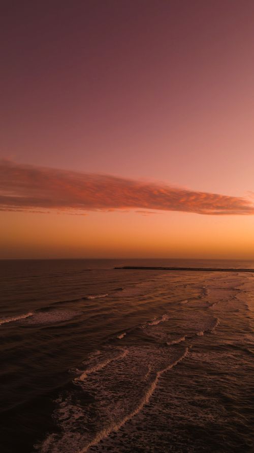 Free Stunning aerial view of a serene ocean with colorful sunset sky. Stock Photo