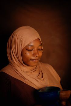 A serene portrait of a woman in a hijab, eyes closed, holding a vessel.