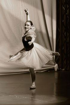 Sepia-toned image of a graceful ballerina performing on stage, showcasing elegance and poise.