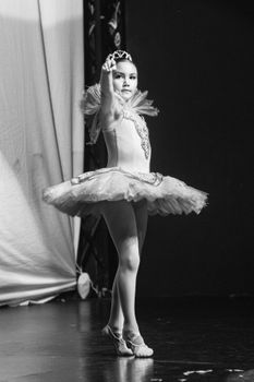 Graceful young ballerina posing on stage in an elegant tutu, black and white.