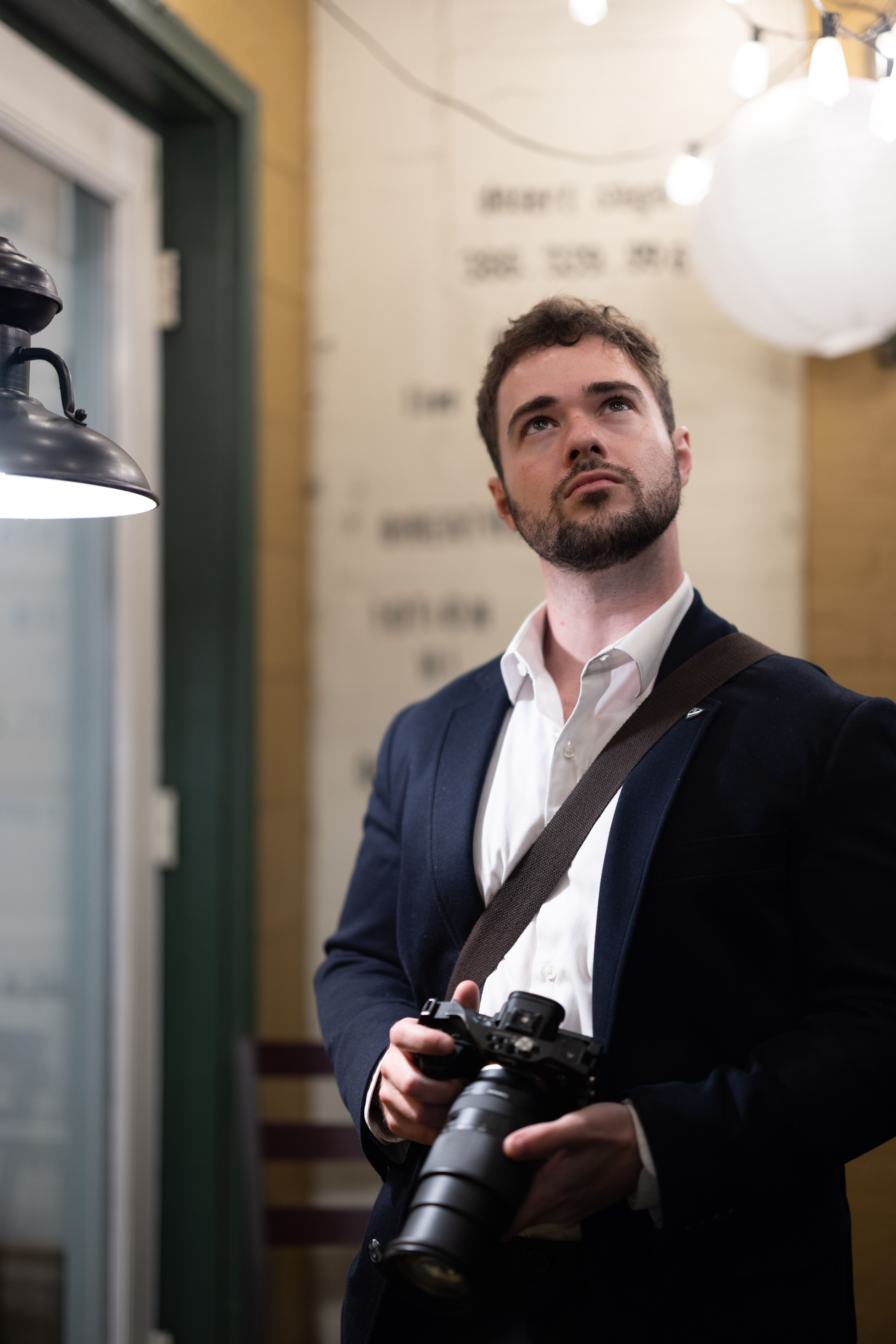 A thoughtful photographer holding a camera indoors, illuminated by warm lighting.