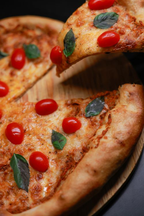 Free Close-up of a fresh Margherita pizza topped with basil and cherry tomatoes on a wooden board. Stock Photo