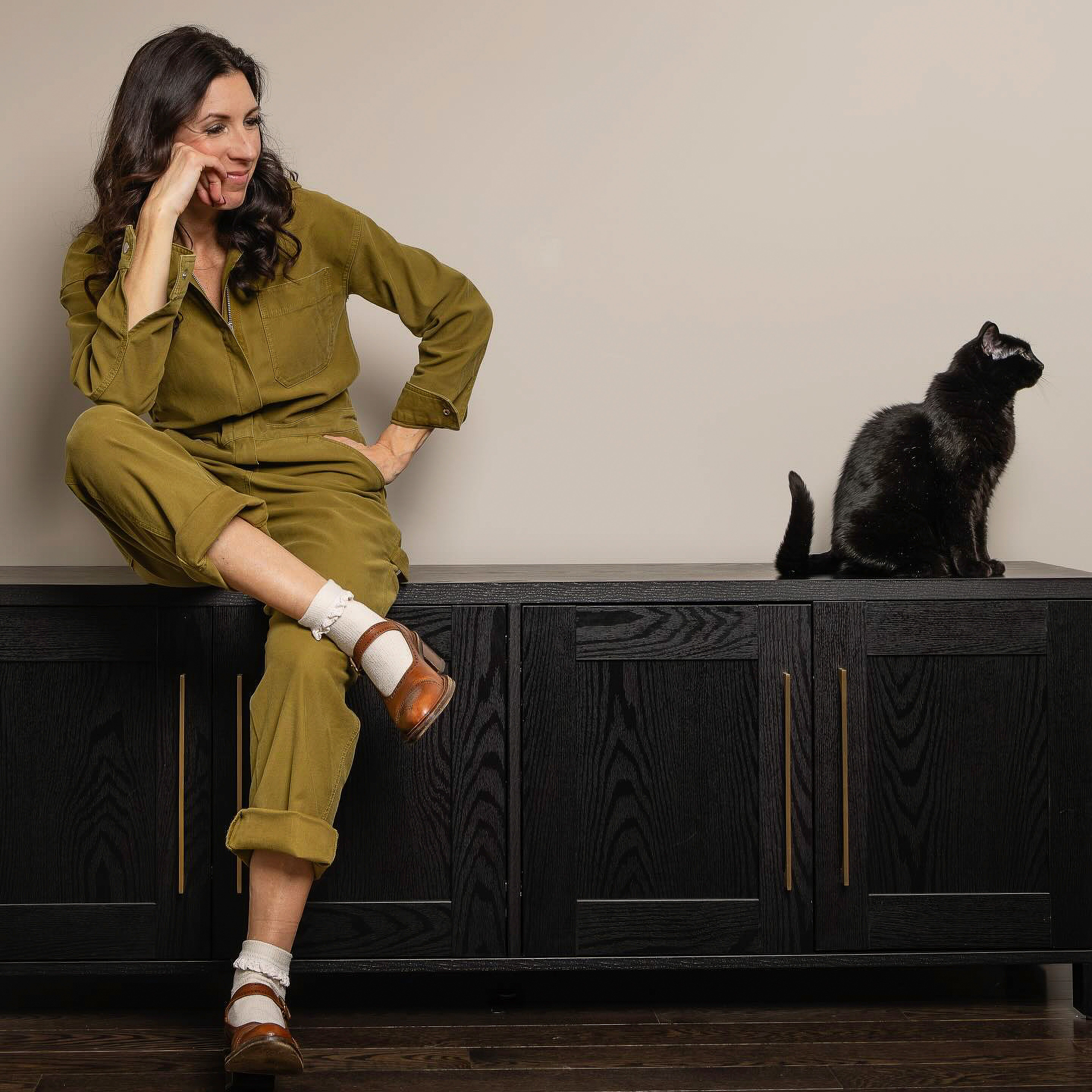 A woman sits with a black cat on a stylish sideboard, showcasing a casual yet modern scene.