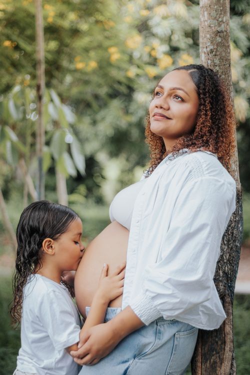Free A heartwarming scene of a daughter kissing her pregnant mother's belly outdoors. Stock Photo