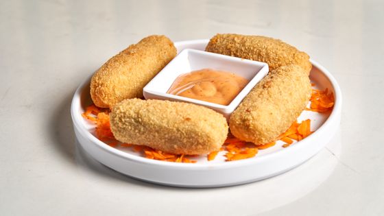 Four golden breadcrumb croquettes around a dish of pink chili mayo on shredded carrot