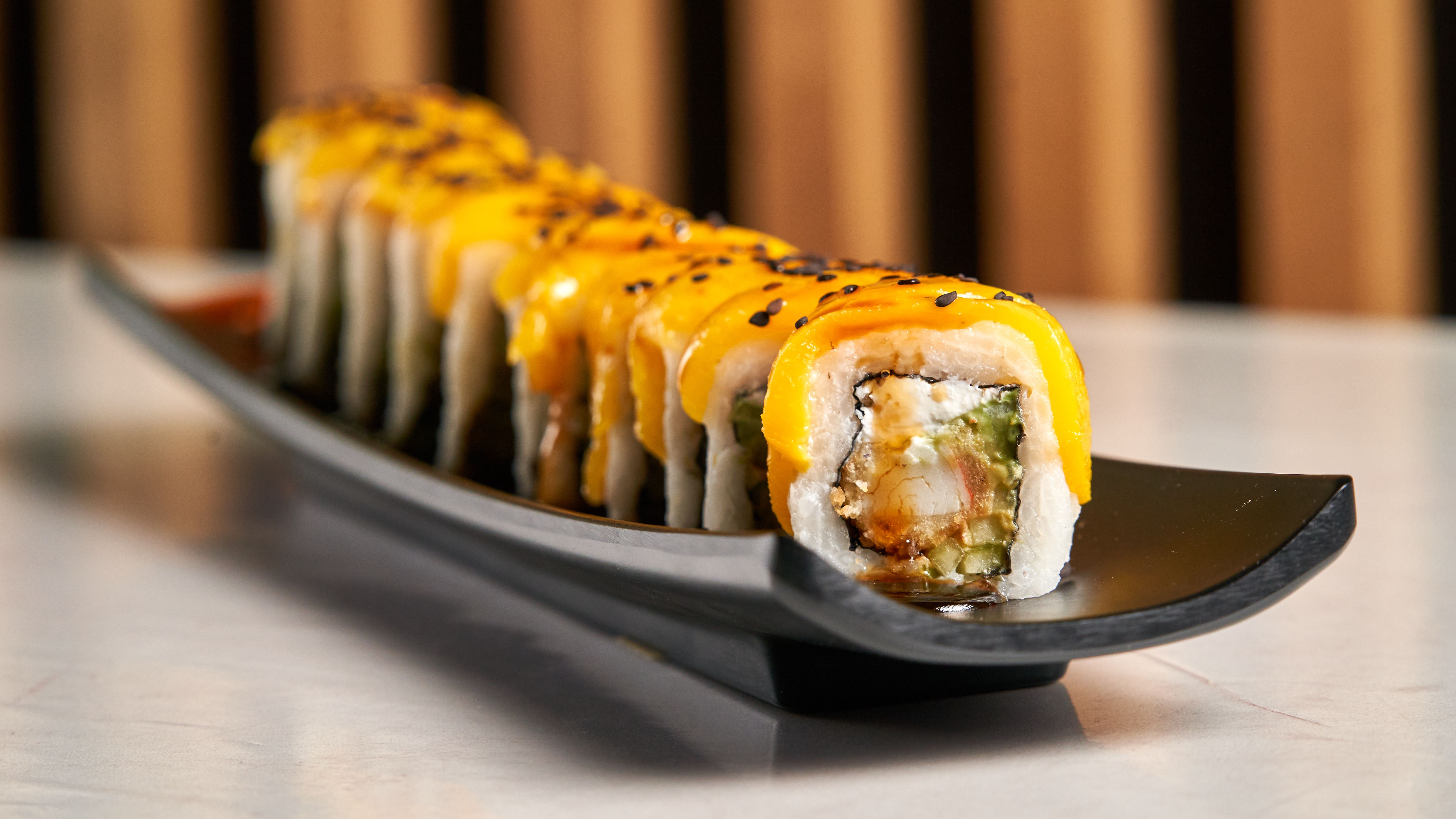 Vibrant mango sushi roll garnished with black sesame seeds on an elegant plate.