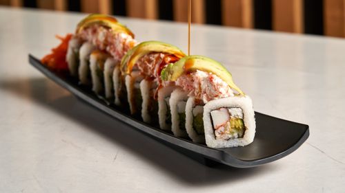 Free Close-up of a sushi roll with avocado and crab, garnished with sauce, served on a black plate. Stock Photo