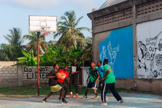 Teenagers playing basketball on an outdoor court with vibrant street art.