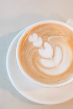 Close-up of a latte with intricate heart-shaped latte art in a white cup and saucer.