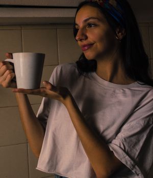 Woman in casual attire holding a white coffee mug, indoors.
