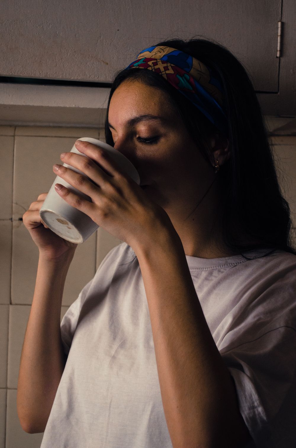 Woman in a headband drinking from a cup in soft shadow