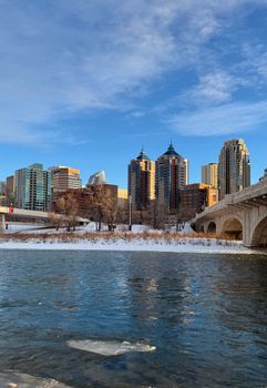 Beautiful view of the Calgary skyline across the Bow River during winter under a clear blue sky.
