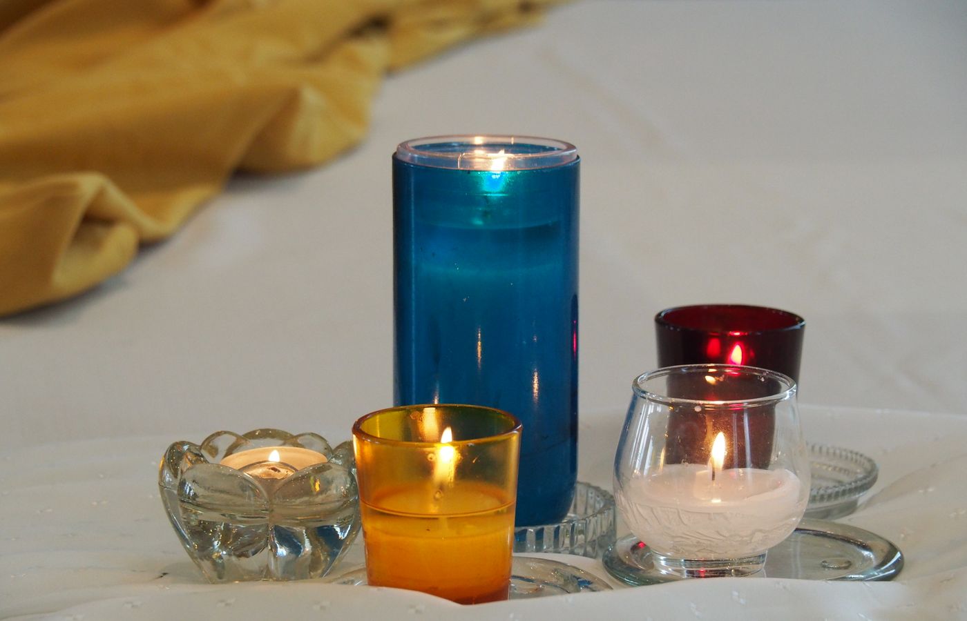 Five colorful candles lit on white linen, creating a warm and serene atmosphere.