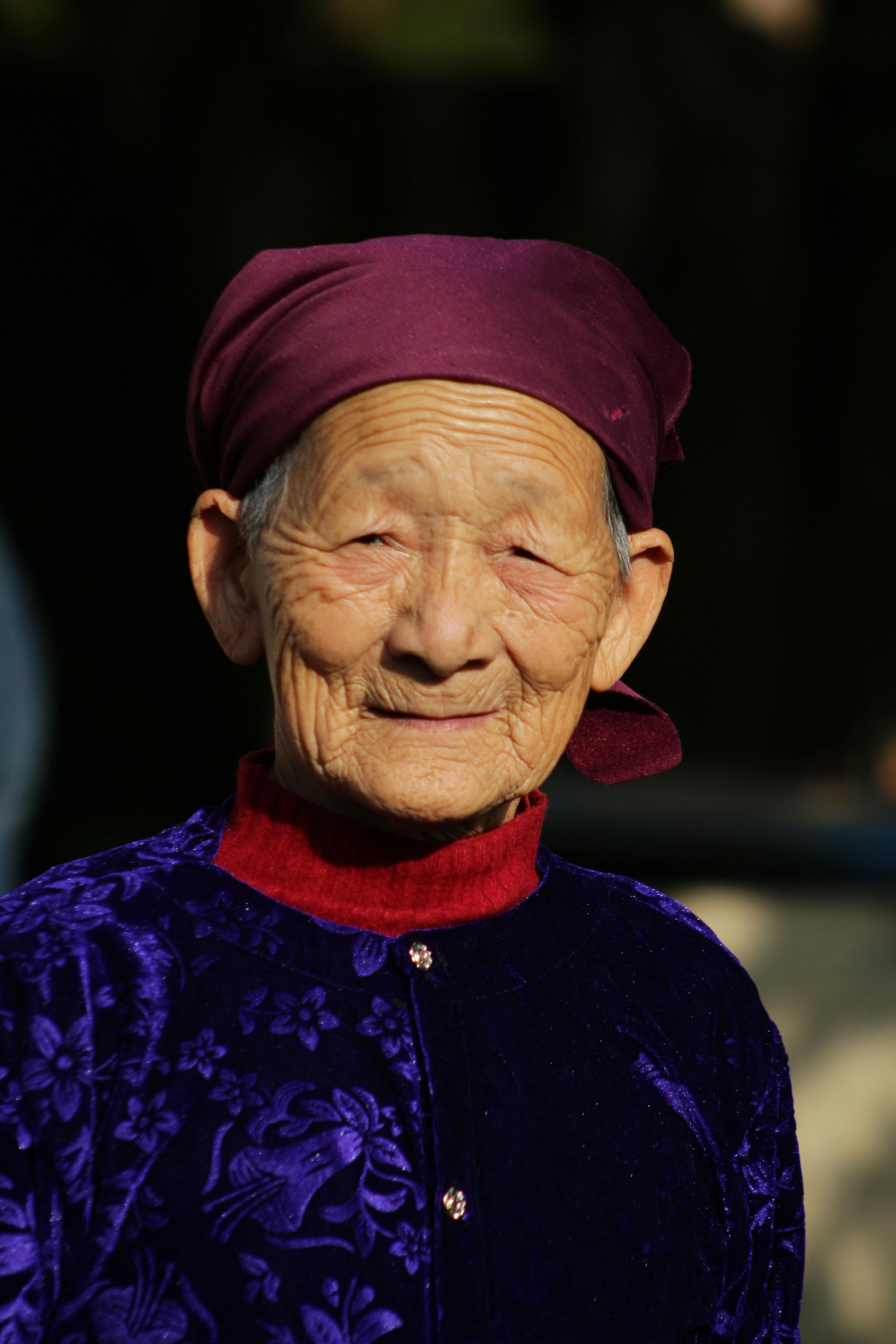Elderly woman in traditional attire with a warm smile, portrait shot outdoors.
