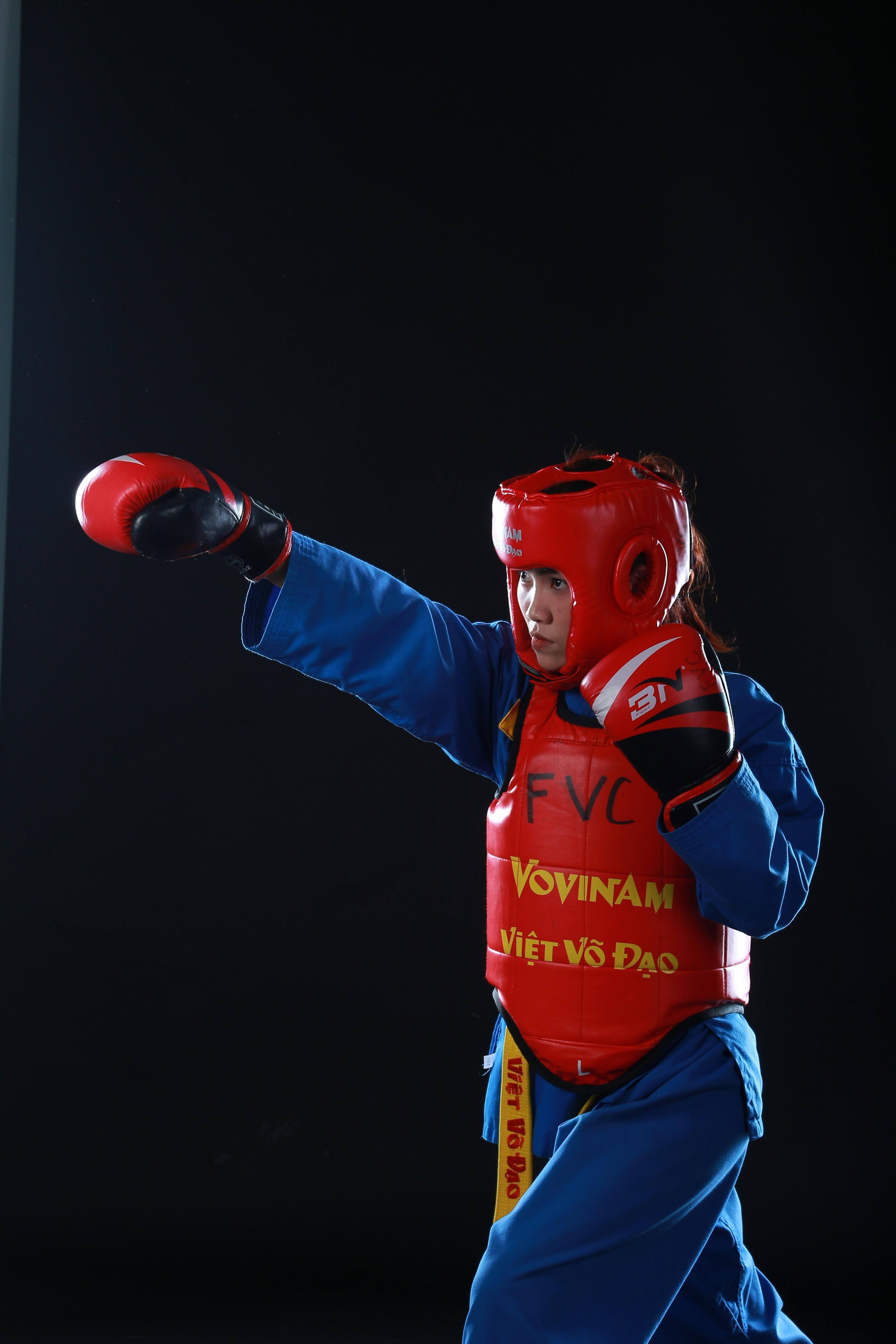A martial artist practicing Vovinam, wearing traditional blue uniform and red protective gear.
