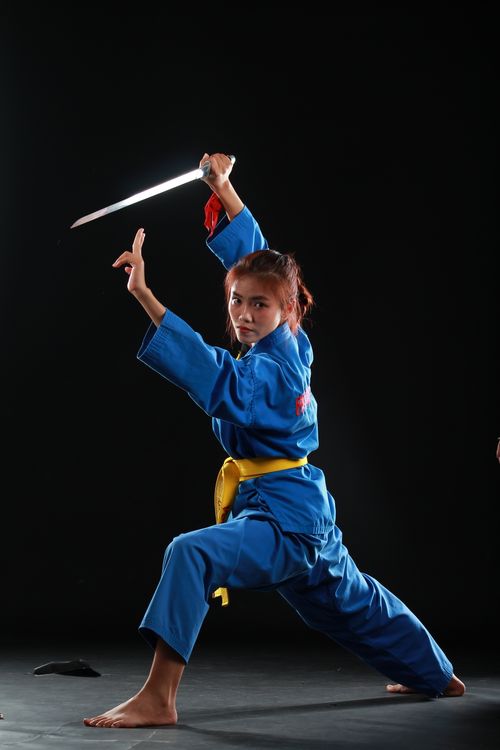 Free Martial artist in blue uniform, striking a powerful pose with a sword in a studio setting. Stock Photo