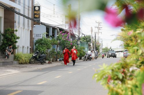Free A couple in traditional red ao dai walking down a lively street, surrounded by greenery. Stock Photo