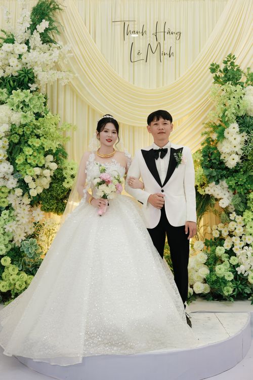 Free Bride and groom in elegant attire posing amid abundant floral decorations indoors. Stock Photo