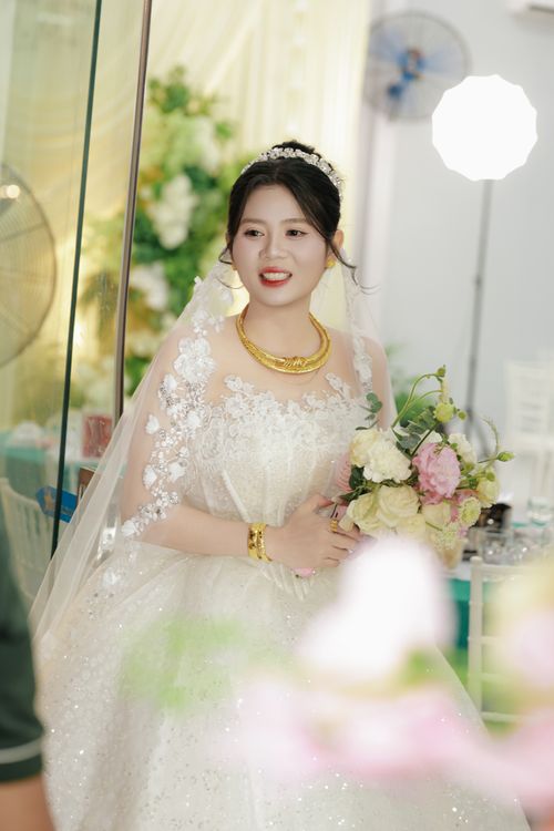 Free Elegant bride in white wedding dress holding floral bouquet, smiling indoors. Stock Photo